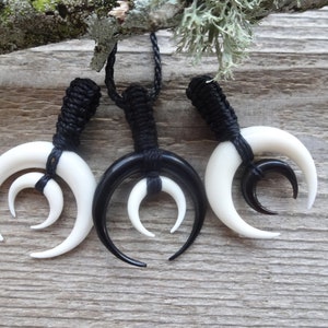 May include: Three black and white bone pendants with a crescent moon shape. The pendants are strung on black cords.