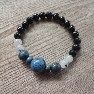 Op de afbeelding: Een armband met zwarte, witte en blauwe kralen met een grote blauwe steen in het midden.