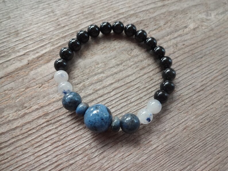 Op de afbeelding: Een armband met zwarte, witte en blauwe kralen met een grote blauwe steen in het midden.