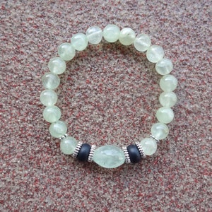 May include: A green gemstone bracelet with silver accents and a larger green gemstone in the center.