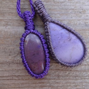 May include: Two purple gemstone pendants with a knotted cord. The pendants are different shapes, one is oval and the other is teardrop.
