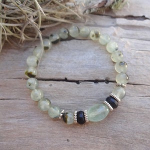 May include: A green and black gemstone bracelet with silver accents. The bracelet is made of round beads and a larger oval bead.