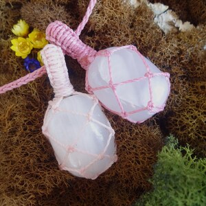 May include: Two pink crystal pendants wrapped in pink macrame cord. The crystals are a light pink color and have a smooth, polished surface. The macrame cord is tied in a knot at the top of each pendant.
