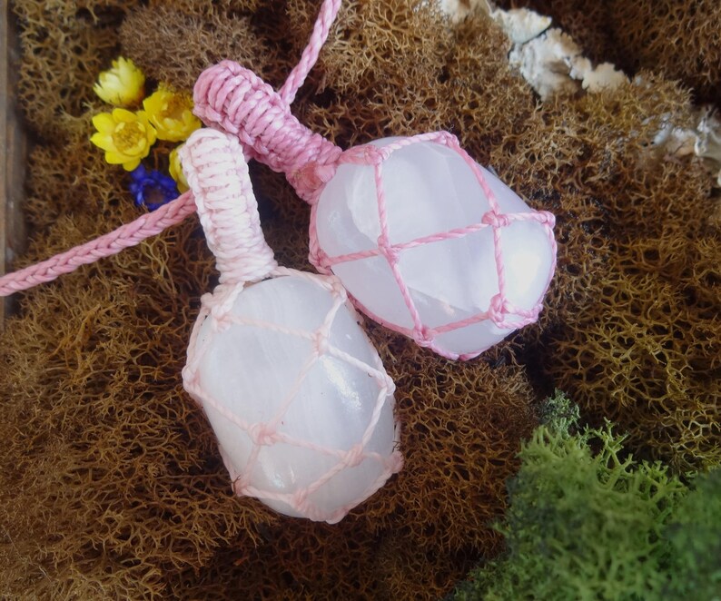 May include: Two pink crystal pendants wrapped in pink macrame cord. The crystals are a light pink color and have a smooth, polished surface. The macrame cord is tied in a knot at the top of each pendant.