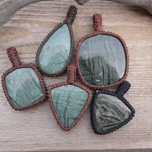May include: Five green and brown stone pendants with intricate patterns, each wrapped in brown or black cord.