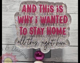 May include: A glittery badge reel with the text "AND THIS IS WHY I WANTED TO STAY HOME all this right here." The text is in pink and black. The badge reel has a pink and white bead.
