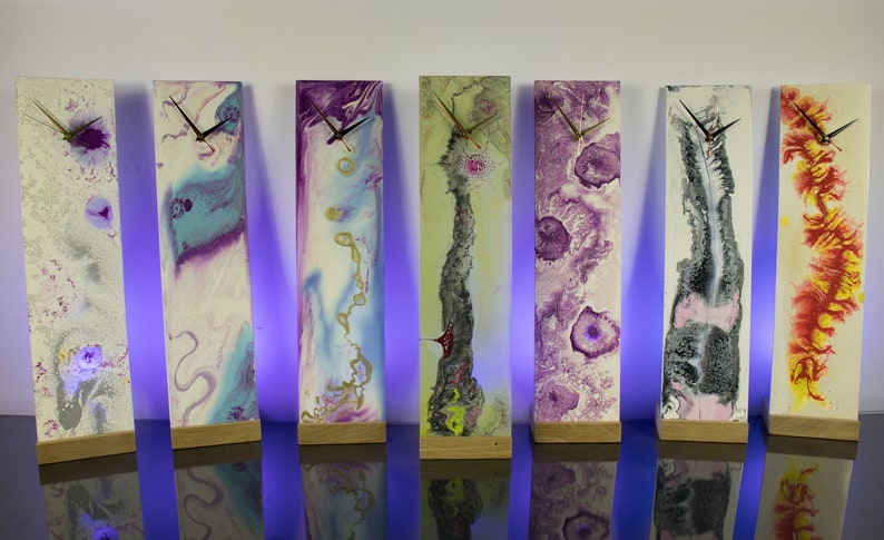 Puede incluir: Seis relojes de arte abstracto con diferentes esquemas de color. Cada reloj est&aacute; montado sobre una base de madera y tiene una esfera blanca con agujas negras.