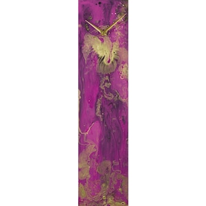 May include: A long, rectangular clock with a pink and gold abstract design. The clock face is white with gold hands.