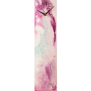Pode incluir: Um relógio retangular alto com um design abstrato rosa, branco e azul. O mostrador do relógio tem ponteiros pretos e detalhes dourados.