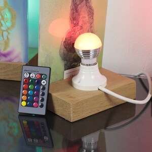 Puede incluir: Una bombilla blanca con un mando a distancia para cambiar el color de la luz. La bombilla est&aacute; sobre una base de madera y est&aacute; conectada a un cable blanco. El mando a distancia tiene una variedad de botones de color, as&iacute; como botones para la luz blanca y un modo de parpadeo.