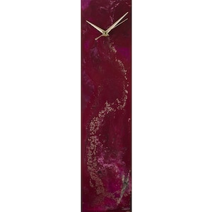 May include: A long, vertical clock with a burgundy background and gold accents. The clock face is white with gold hands.