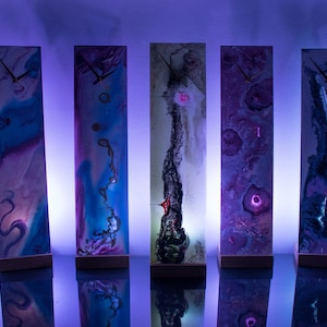 May include: Eight tall, rectangular clocks with unique abstract designs. Each clock has a white background with colorful, swirling patterns and a gold clock face.
