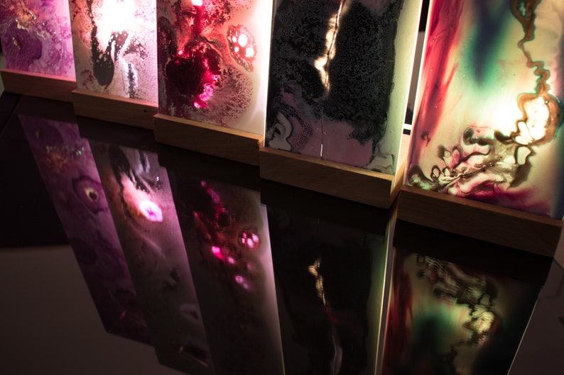 Op de afbeelding: Vier rechthoekige lichtbakken met abstracte ontwerpen in tinten roze, paars, groen en zwart. De lichtbakken worden van achteren verlicht, waardoor een gloeiend effect ontstaat.