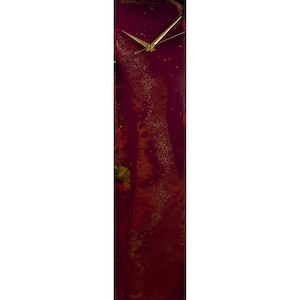 May include: A tall, rectangular clock with a burgundy background and gold accents. The clock face has gold hands and a white background.