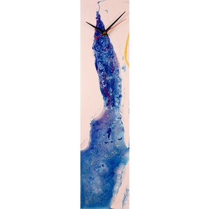 Pode incluir: Um relógio vertical longo com fundo rosa e um design abstrato azul. Os ponteiros do relógio são pretos.