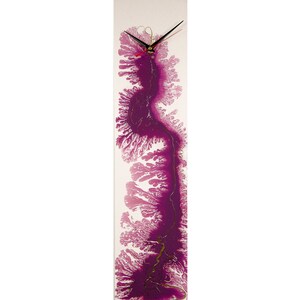 May include: A long, rectangular clock with a white background and a purple abstract design. The clock hands are black and red.