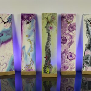 Puede incluir: Seis relojes rectangulares altos con dise&ntilde;os de arte abstracto, coloridos y fluidos. Cada reloj tiene una base de madera y una esfera blanca con manecillas negras.