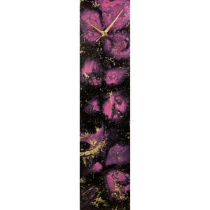Pode incluir: Um relógio retangular longo com fundo preto e design abstrato rosa e dourado. O relógio tem ponteiros dourados.