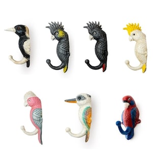 May include: Set of seven bird-shaped hooks, each with a different colour and design. The hooks are made of metal and have a J-shape. The birds include a black and white kookaburra, a black cockatoo, a yellow cockatoo, a pink galah, a kingfisher, and a red and blue bird.