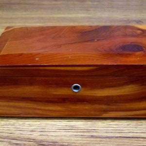 May include: A wooden box with a natural cedar finish. The box has a small hole on the front.