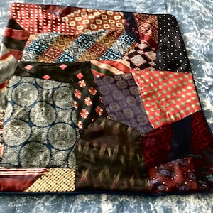 May include: A patchwork pillow cover made from repurposed ties. The pillow cover features a variety of colors and patterns, including red, blue, green, and black. The ties are sewn together in a random pattern, creating a unique and eye-catching design.