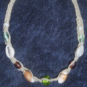 May include: A beige crocheted necklace with green, brown, and white beads and shells.