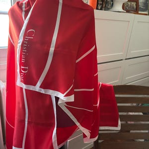May include: A red and white silk scarf with the text "Christian Dior" printed on it.