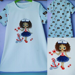 May include: White t-shirt with a blue and white striped sleeve. The front of the shirt features a cartoon girl wearing a sailor hat and holding a star. The girl is standing next to an anchor.