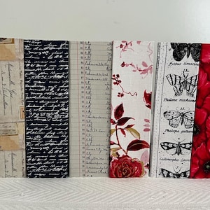 May include: A collection of decorative bookmarks with various patterns. Designs include the Eiffel Tower, vintage postcards, script, ledger paper, floral, butterflies, red poppies, and daisies. Each bookmark is rectangular and stands upright.
