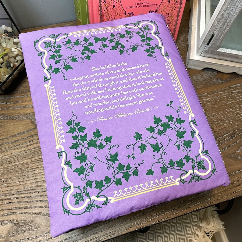 May include: A purple book cover with a green ivy design and white text. The text reads "She held back the swinging curtain of ivy and pushed back the door which opened slowly-slowly. Then she slipped through it, and shut it behind her, and stood with her back against it, looking about her and breathing quite fast with excitement, and wonder, and delight. She was standing inside the secret garden."  Frances Hodgson Burnett