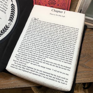 May include: A close-up of a book with a white cover and black text. The text reads "Chapter 1 There is No One Left". The book is open to a page with text about a young girl named Mary Lennox who is sent to live with her uncle at Misselthwaite Manor.
