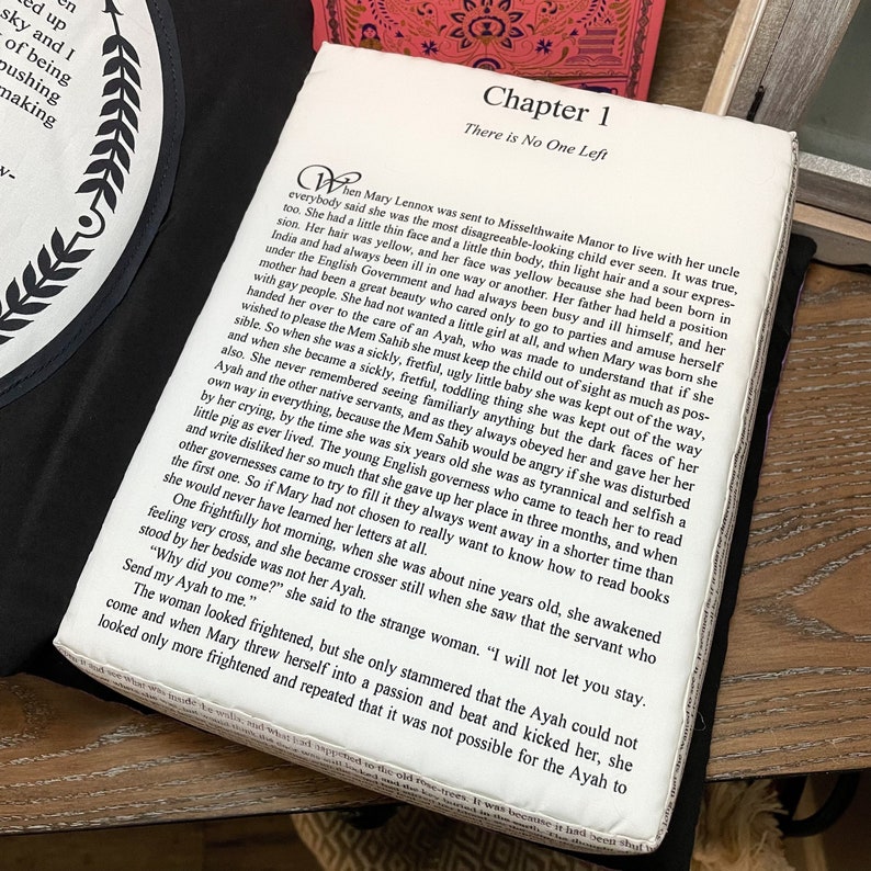May include: A close-up of a book with a white cover and black text. The text reads "Chapter 1 There is No One Left". The book is open to a page with text about a young girl named Mary Lennox who is sent to live with her uncle at Misselthwaite Manor.