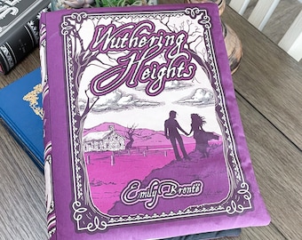 May include: A purple book with a black spine and a white and black illustration of a house and two figures on the front cover. The title "Wuthering Heights" is written in white and black lettering. The author "Emily Brontë" is written in white lettering below the illustration.