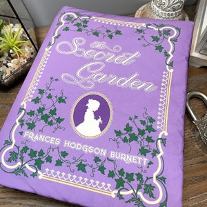 May include: A purple book cover with a white silhouette of a girl and the text "The Secret Garden" by Frances Hodgson Burnett. The cover is decorated with green ivy.