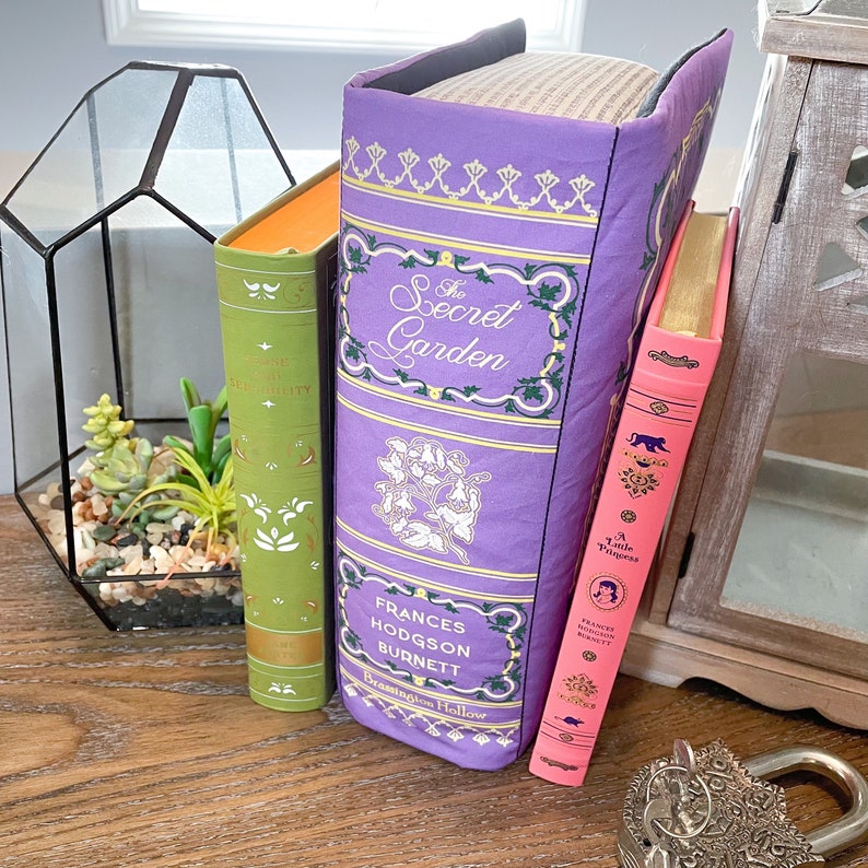 May include: Three hardcover books with purple, green, and pink covers. The purple book has the title "The Secret Garden" and the author "Frances Hodgson Burnett". The green book has the title "Pride and Prejudice" and the author "Jane Austen". The pink book has the title "A Little Princess" and the author "Frances Hodgson Burnett".
