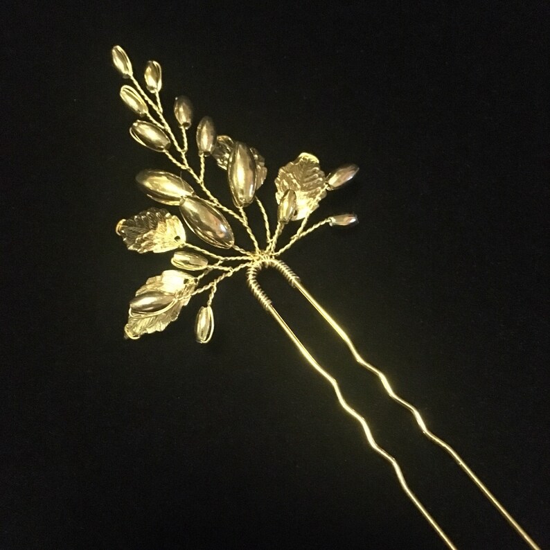 May include: Gold hair comb with a floral design. The comb has a long, double-pronged stem and features delicate leaves and oval-shaped beads.