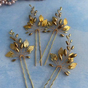 May include: Three gold hair pins with leaf and bead embellishments. The pins are wavy and have a gold finish.