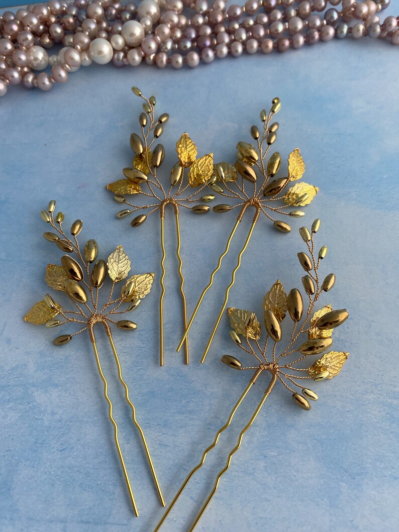 May include: Three gold hair pins with leaf and bead embellishments. The pins are wavy and have a gold finish.