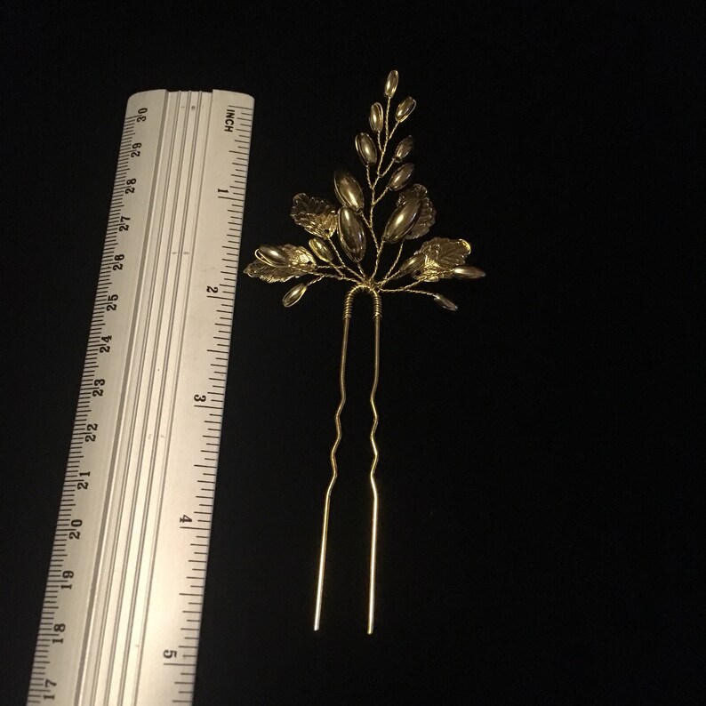 May include: Gold hair pin with a floral design. The pin is about 4 inches long and has a delicate, intricate design.