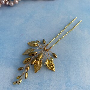 May include: Gold hair pin with a delicate design of leaves and beads. The pin is made of wire and has a simple, elegant look.
