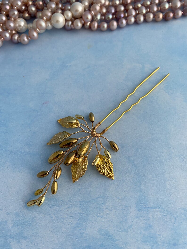 May include: Gold hair pin with a delicate design of leaves and beads. The pin is made of wire and has a simple, elegant look.