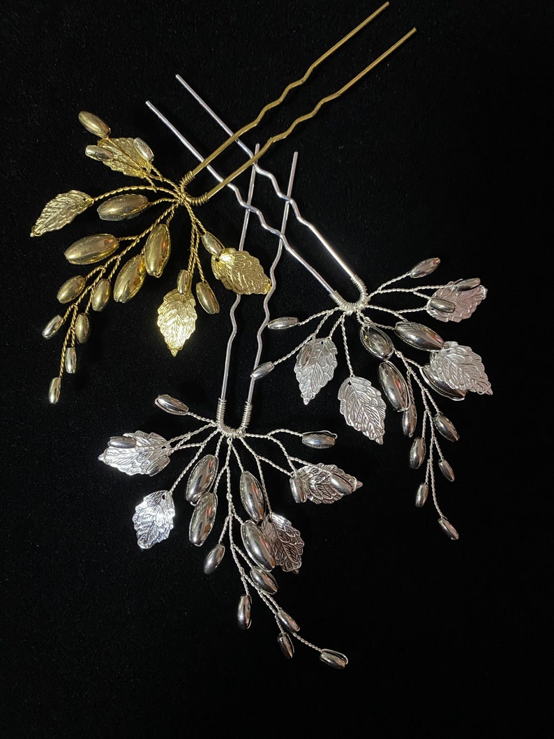 May include: Three gold and silver hair pins with leaf and bead accents. The pins are arranged in a starburst pattern on a black background.