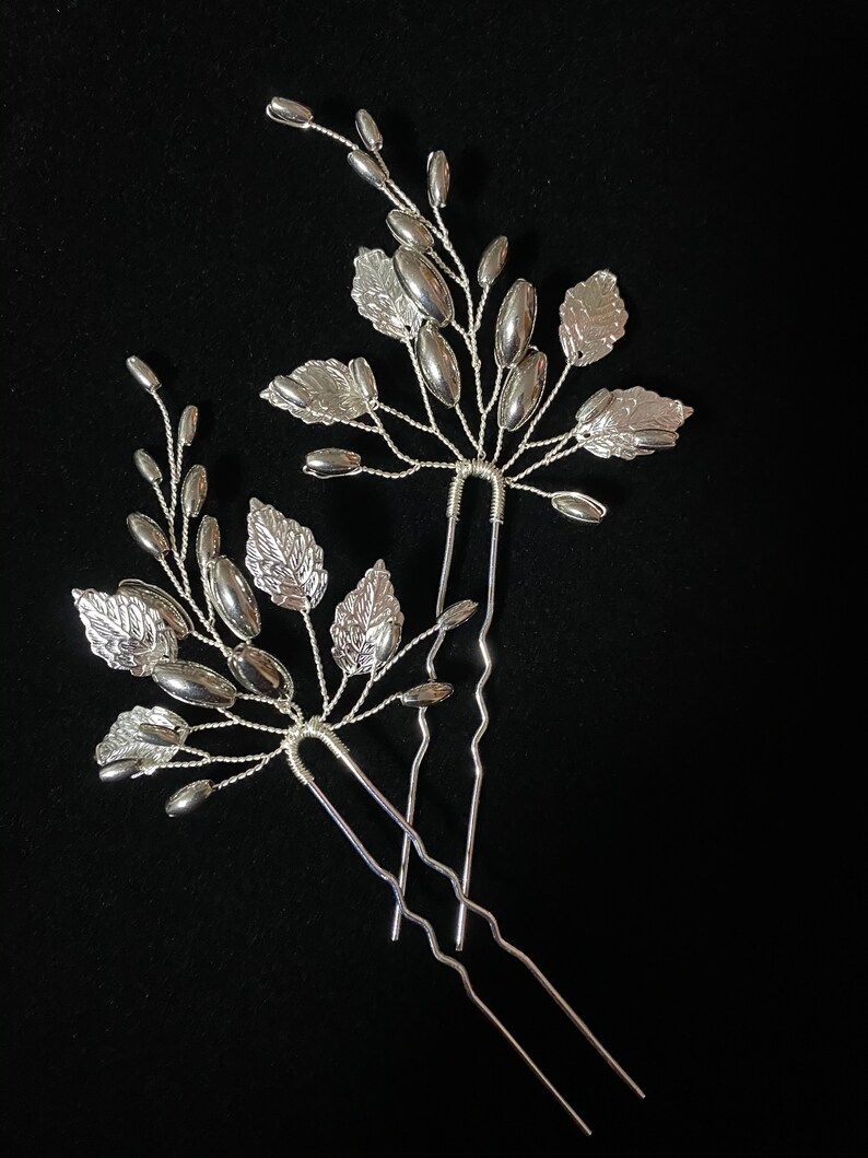 May include: Three silver hair pins with decorative leaf and bead accents. The pins are arranged in a fan shape.