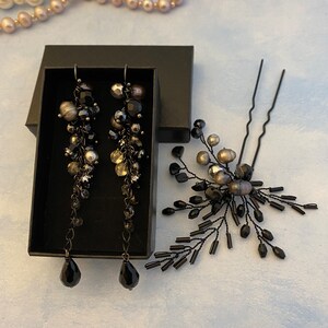 Könnte beinhalten: Ein schwarzes Schmuckset mit langen Ohrhängern mit schwarzen Tropfenanhängern und einer passenden Haarnadel. Die Ohrringe befinden sich in einer schwarzen Schachtel, und die Haarnadel hat ein florales Design mit schwarzen Perlen und Perlen. Perlenketten sind im Hintergrund.
