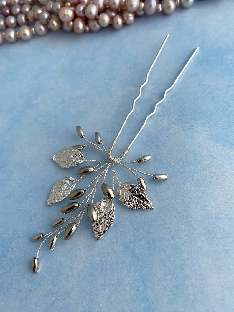 May include: Silver hair comb with a delicate design of leaves and beads. The comb has two prongs for easy insertion into hair.