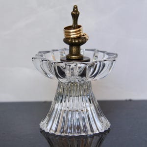 May include: A clear glass ring holder with a fluted base and a decorative brass top. Two gold rings rest on the top. The ring holder is designed to display and store rings.