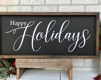 May include: A wooden sign with a black background and white lettering that reads "Happy Holidays". The sign is sitting on a wooden stand in front of a brick wall.