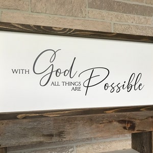 May include: A wooden framed sign with the text "With God All Things Are Possible" in black cursive lettering on a white background.