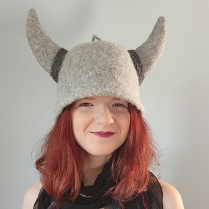 May include: A gray felt Viking hat with horns. The hat is worn by a person with long red hair.