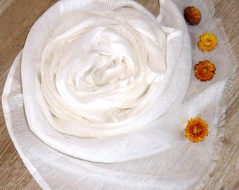 May include: A white sheer scarf with a fringed edge. The scarf is rolled up and decorated with four small, dried orange flowers.